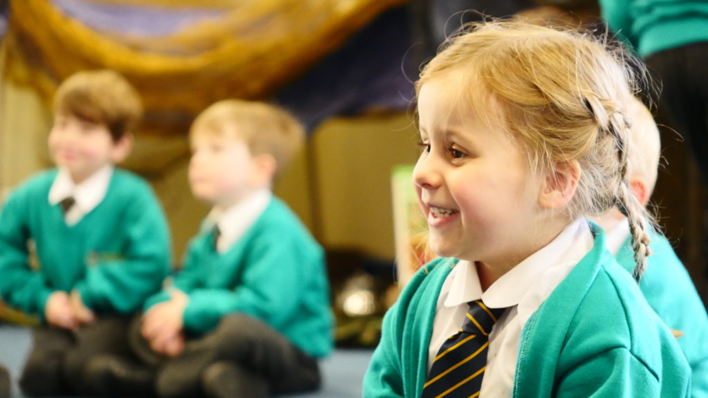 A beautiful little girl sitting on the floor with her legs crossed while listening to the teacher.