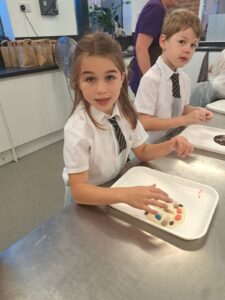 Two Year 4 pupils are pictured smiling for the camera whilst wearing aprons and making chocolate together.