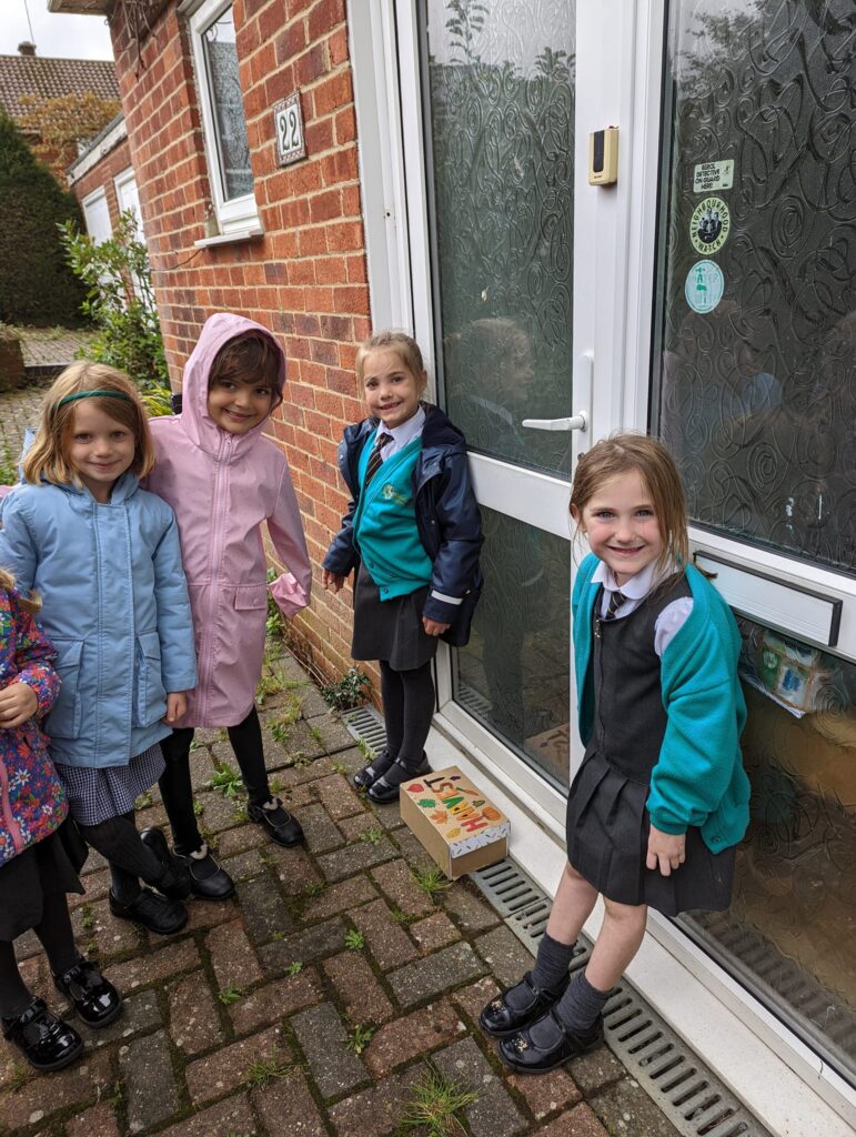 4 children stood in front of a building with a harvest box on the floor