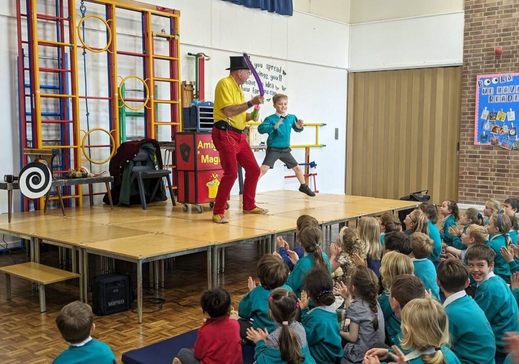 Photo taken of the Magic Show, organised by FoHPS, with a young male pupil seen participating in a trick with the magician.