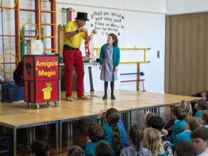 Photo taken of the Magic Show, organised by FoHPS, with a young female pupil seen participating in a trick with the magician.