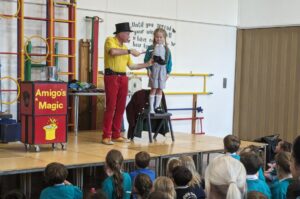 Photo taken of the Magic Show, organised by FoHPS, with a young female pupil seen participating in a trick with the magician.