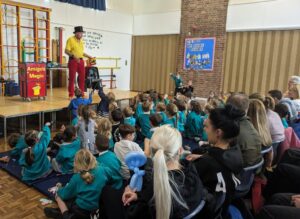 Photo taken of the Magic Show, organised by FoHPS, with several pupils holding up their hands to participate in a trick with the magician.