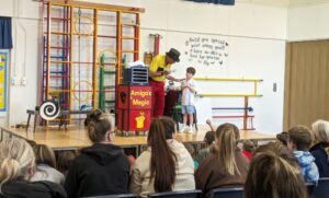 Photo taken of the Magic Show, organised by FoHPS, with a young male pupil seen participating in a trick with the magician.