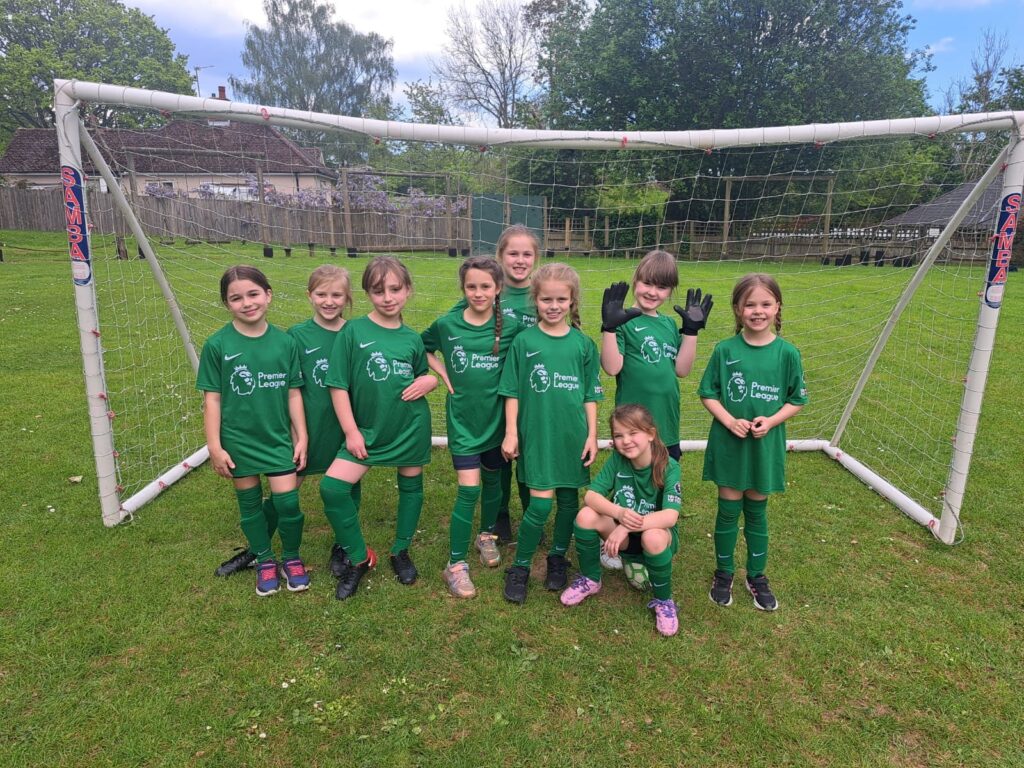 A group of female pupils are pictured smiling together for the camera in front of a goalpost, having just won a Football match.