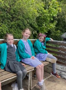 Three female pupils are pictured sat together on a wooden bench on a balcony overlooking a canal, during a school trip to Kent Life.